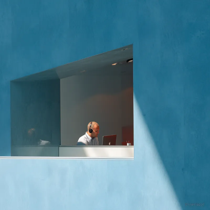 Man Working on Laptop in Minimalist Blue Window