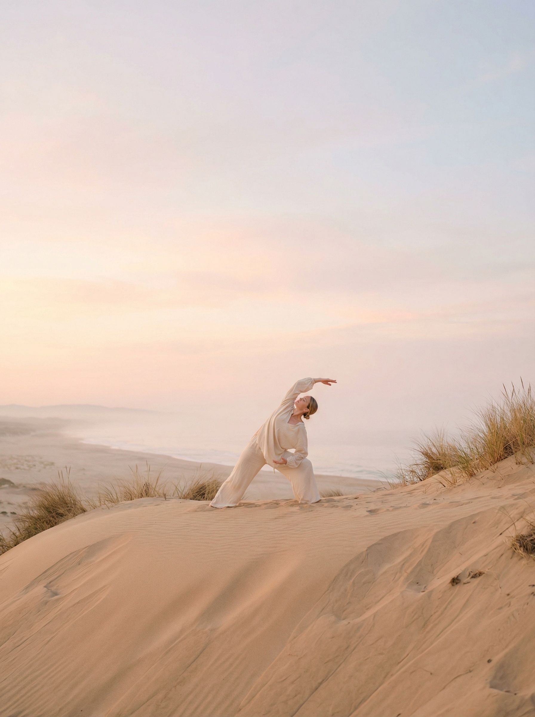 Woman stretching on sandy dune at sunrise