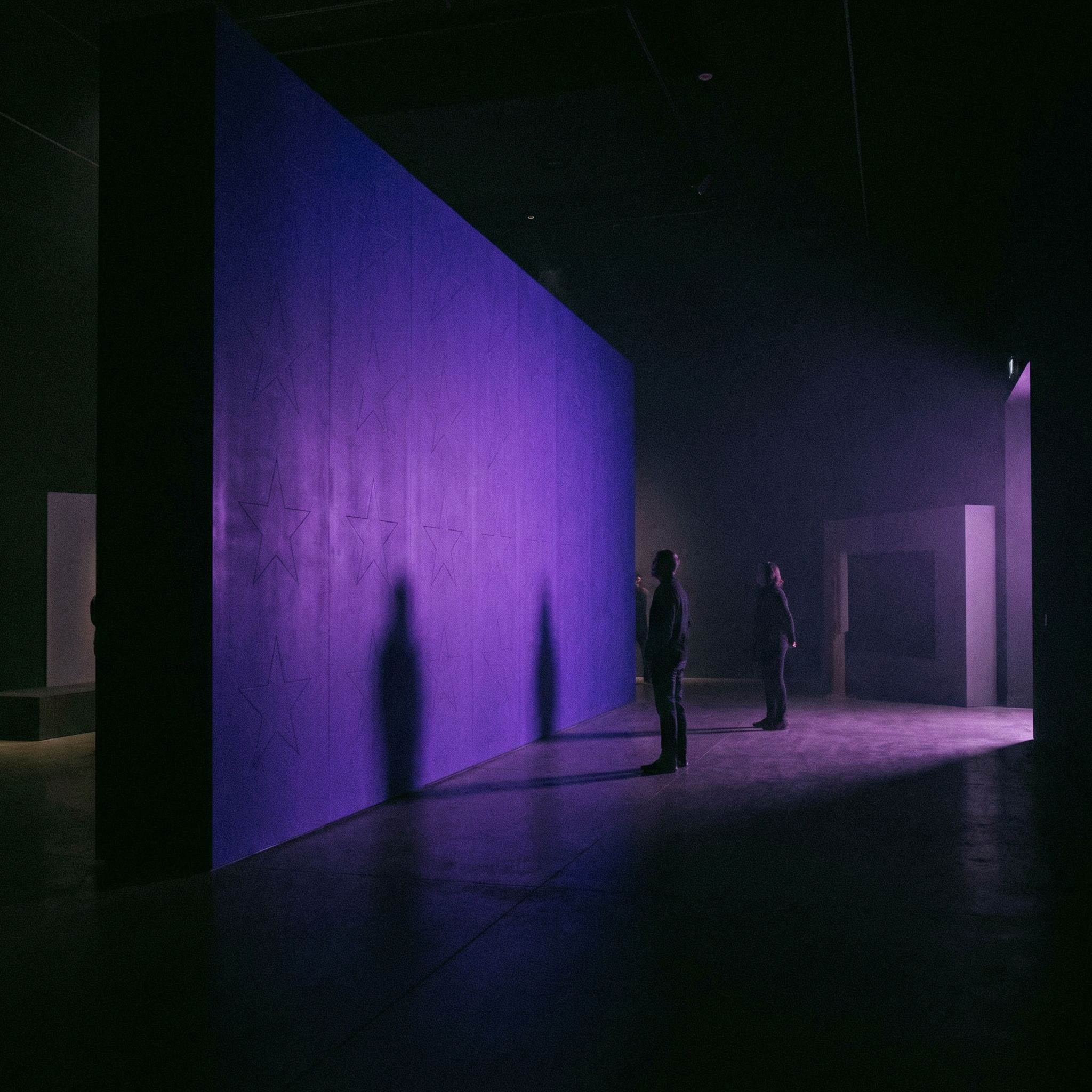 People observing purple illuminated wall in gallery