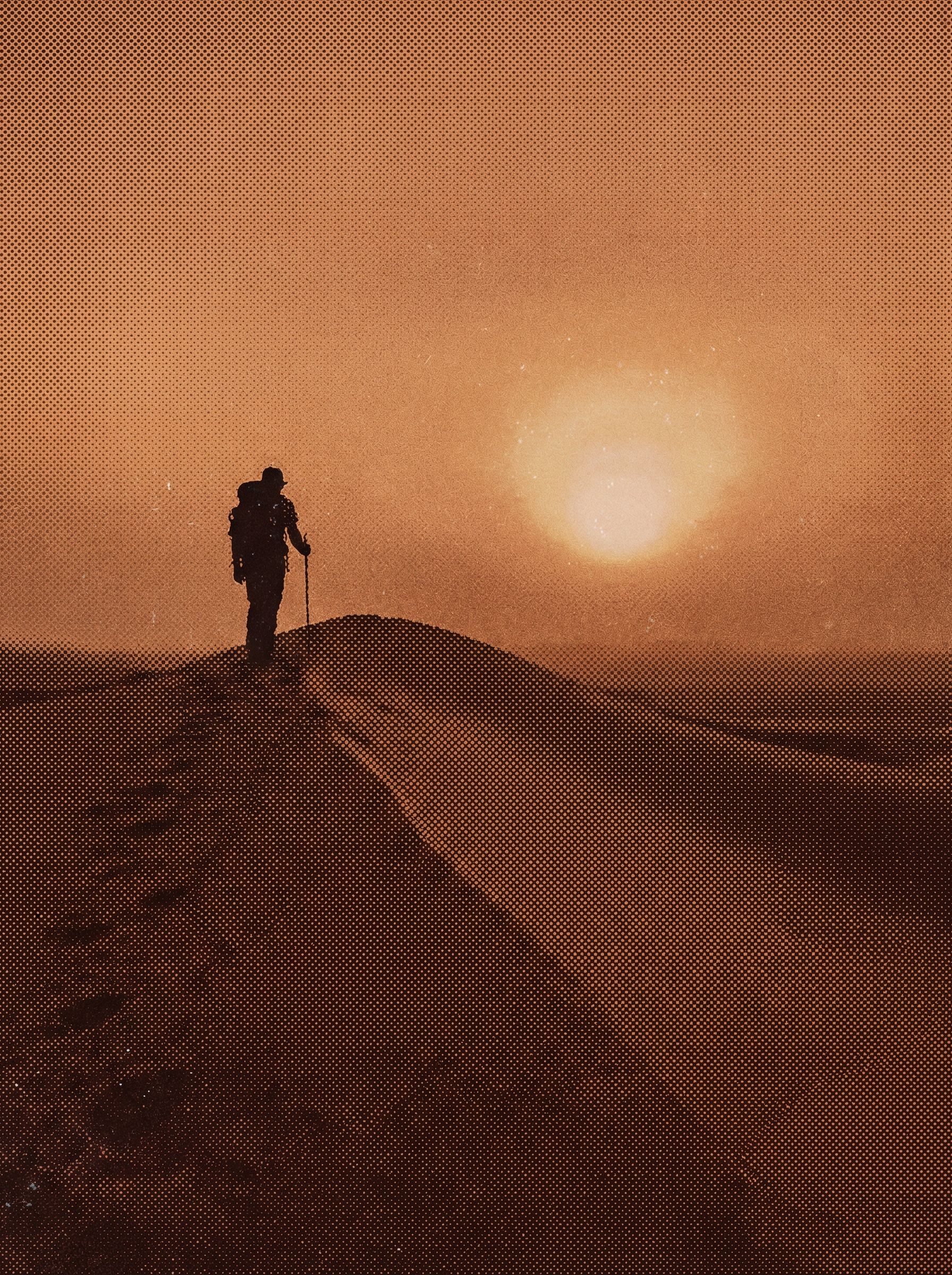 Lone hiker on desert dune at sunset