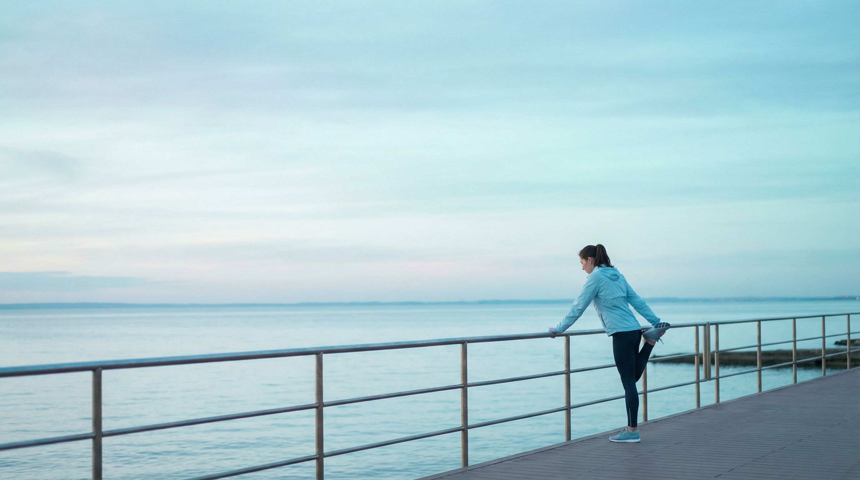 Woman stretching on seaside boardwalk at dawn