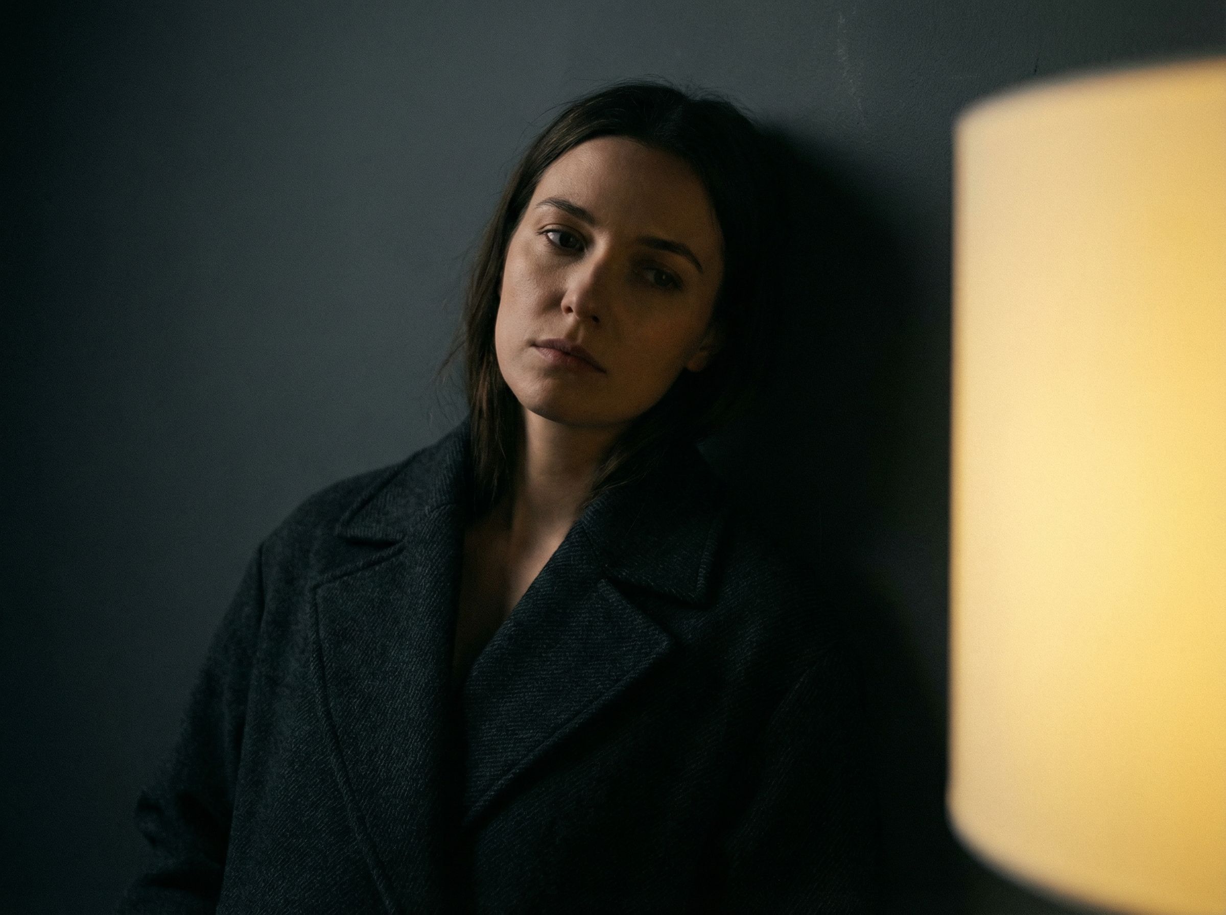 Pensive woman leaning against dark wall