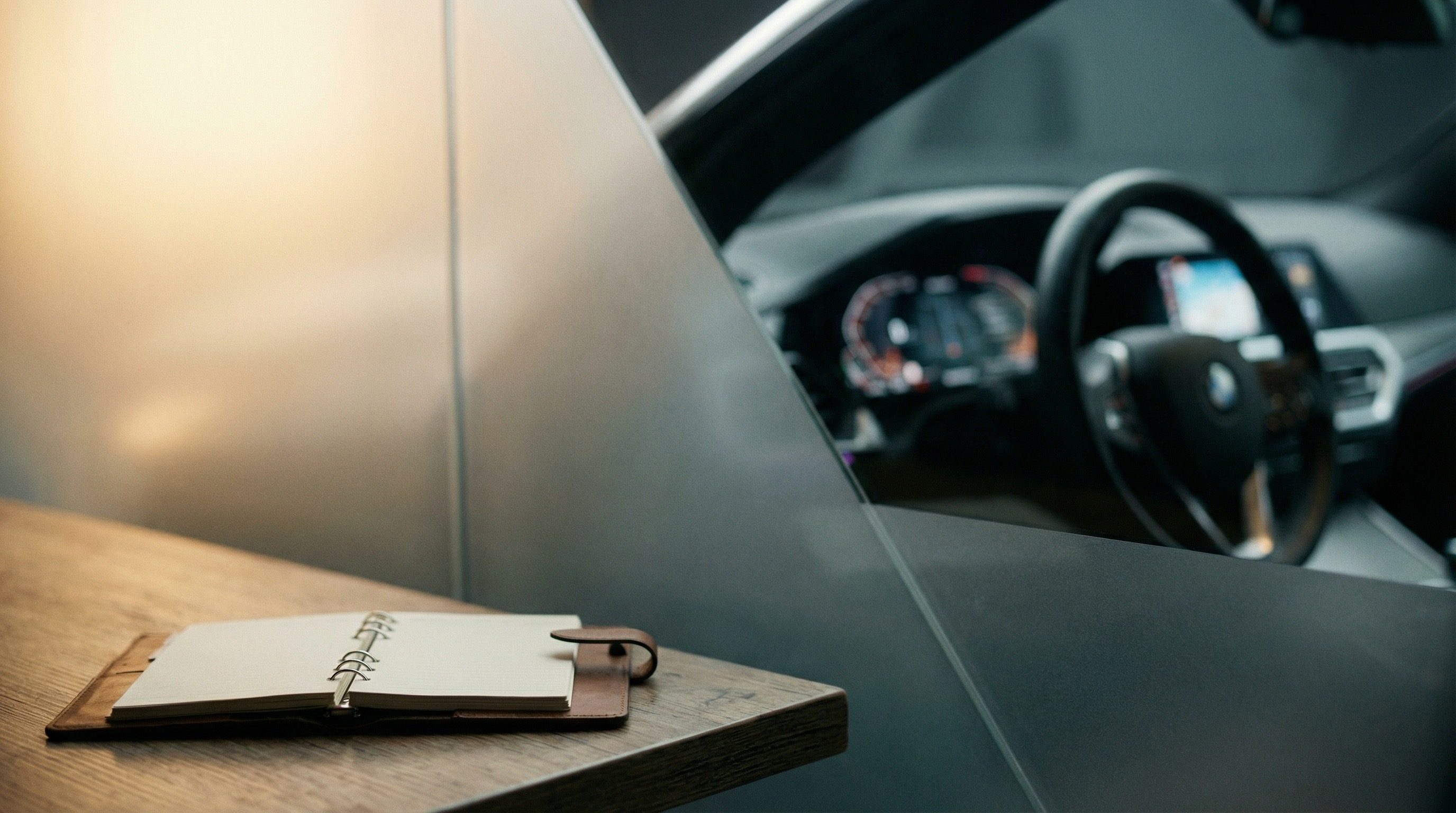 Open notebook on wooden desk near modern car