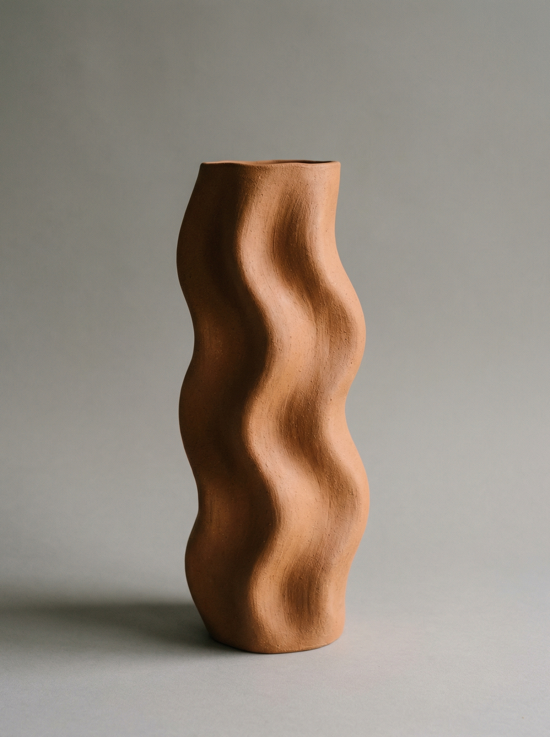 Wavy terracotta ceramic vase on gray background