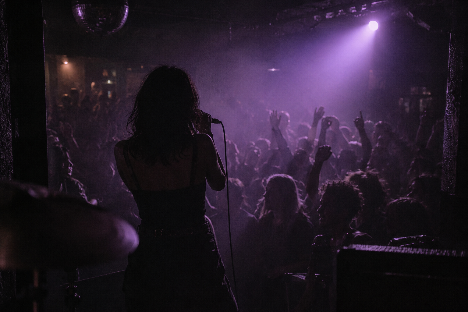 A singer facing a small crowd under a violet spotlight
